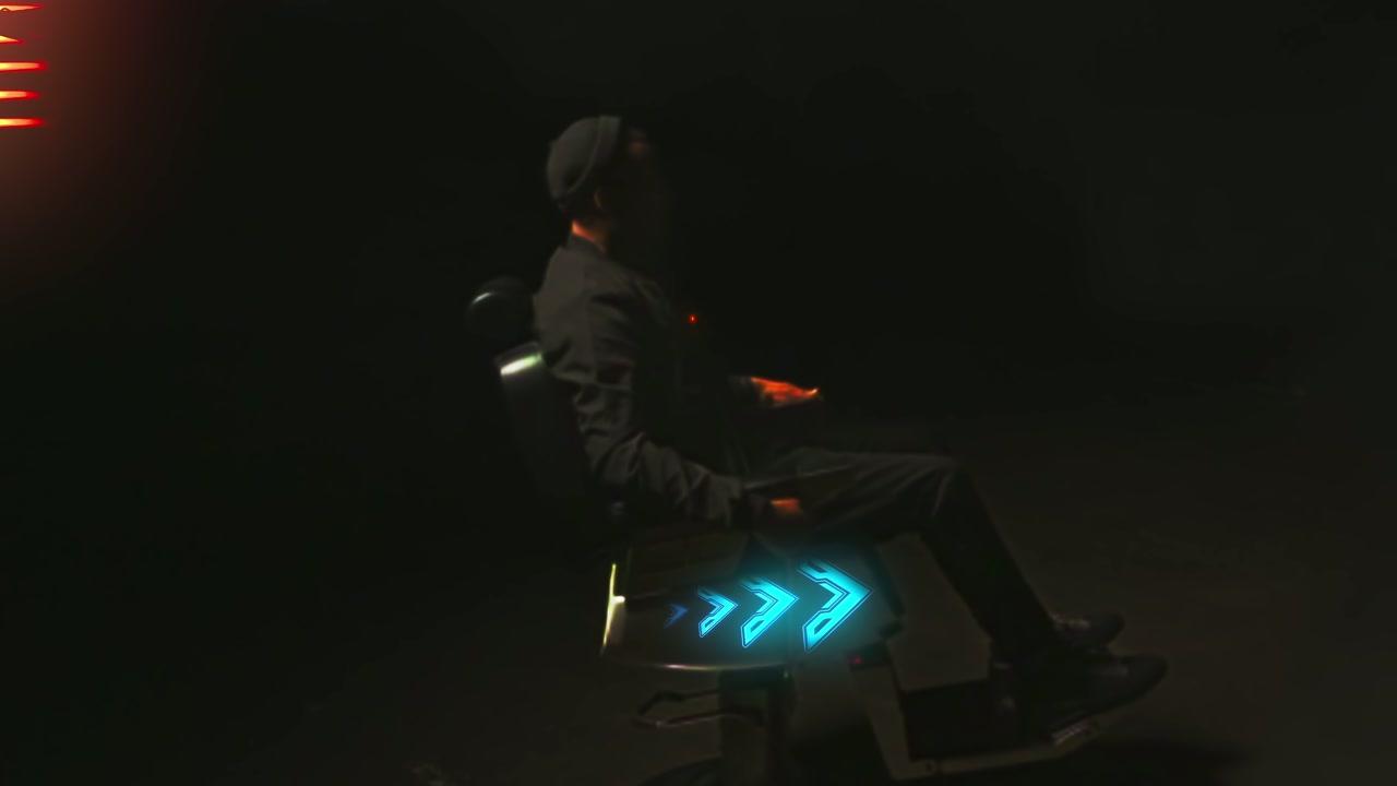 A seated figure in near darkness, cyan light raking across the frame